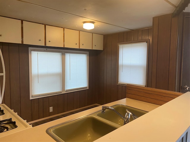 kitchen featuring gas cooktop, white cabinets, sink, and wood walls