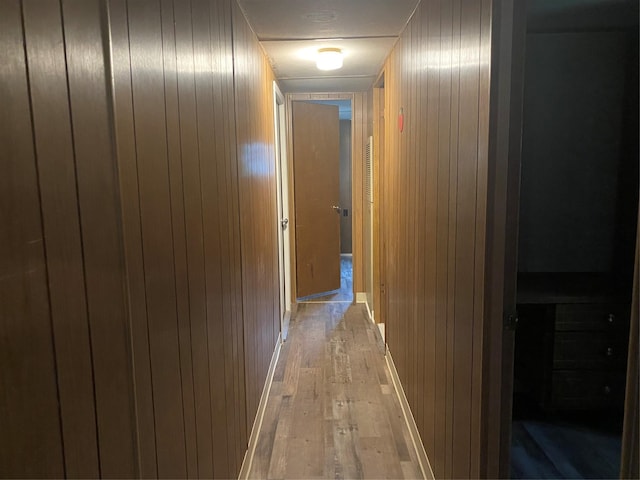 hallway featuring light wood-type flooring and wood walls