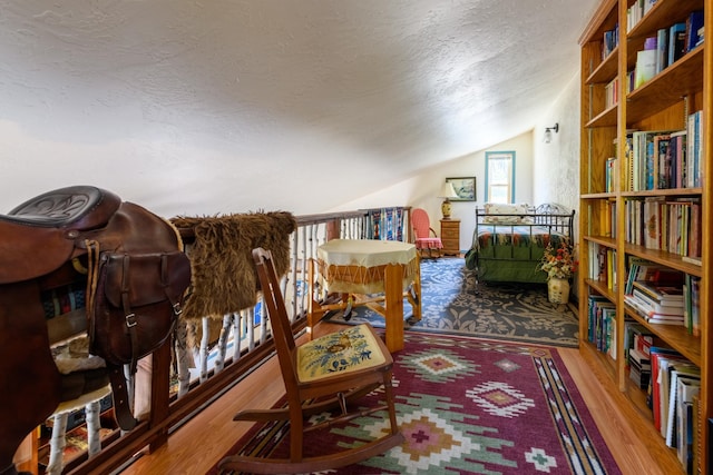 sitting room with a textured ceiling, light wood-type flooring, and lofted ceiling