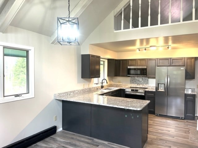 kitchen featuring stainless steel appliances, kitchen peninsula, sink, light stone countertops, and light hardwood / wood-style floors