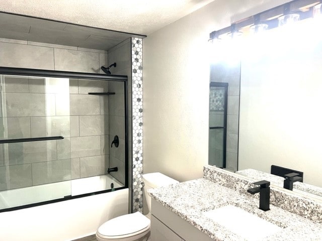 full bathroom with shower / bath combination with glass door, vanity, toilet, and a textured ceiling