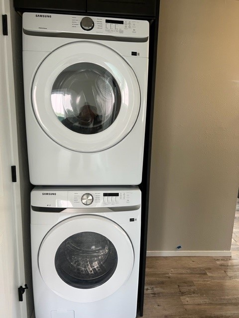 clothes washing area featuring stacked washing maching and dryer and wood-type flooring