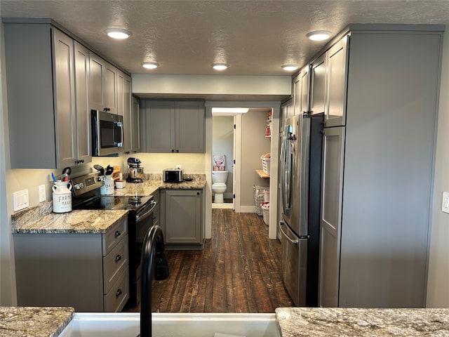 kitchen with a textured ceiling, stainless steel appliances, dark wood-type flooring, gray cabinets, and light stone countertops