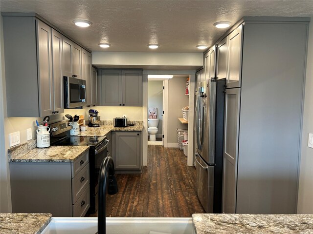 kitchen featuring a textured ceiling, gray cabinetry, dark hardwood / wood-style flooring, stainless steel appliances, and light stone counters