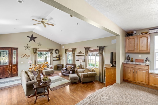 living room with ceiling fan, vaulted ceiling, light hardwood / wood-style floors, and a textured ceiling