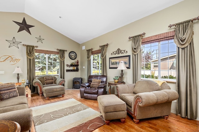 living room with high vaulted ceiling, a healthy amount of sunlight, hardwood / wood-style floors, and a wood stove