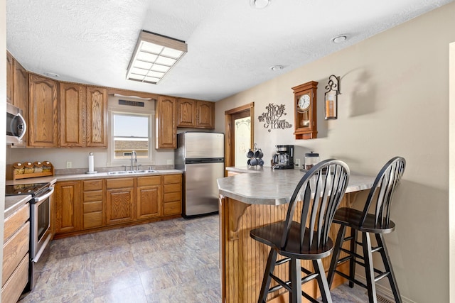 kitchen with sink, a kitchen bar, kitchen peninsula, stainless steel appliances, and a textured ceiling