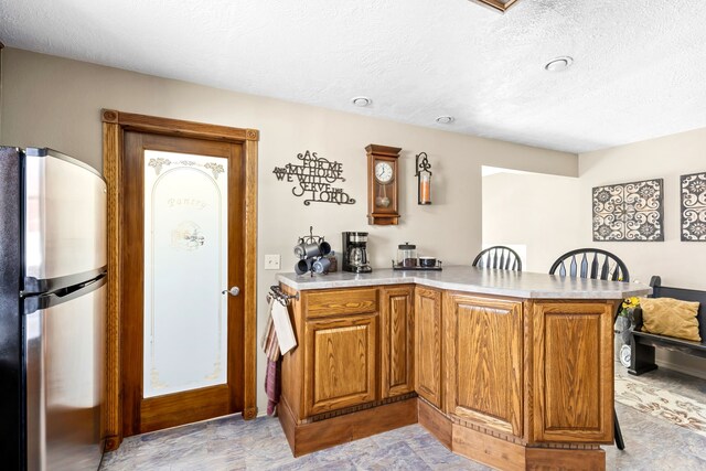 kitchen featuring a breakfast bar area, a textured ceiling, stainless steel refrigerator, and kitchen peninsula