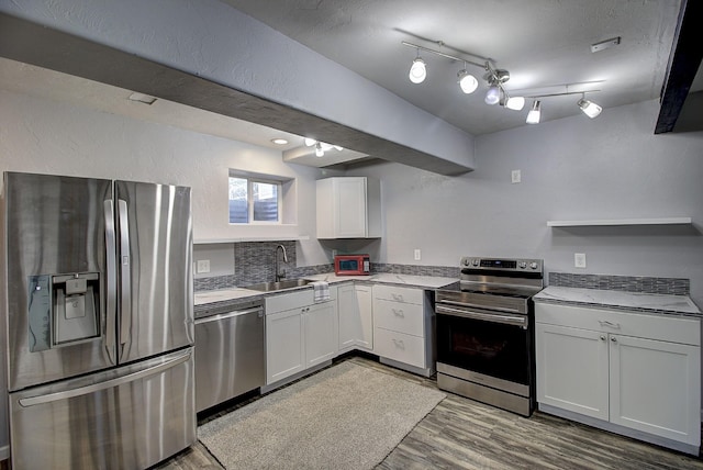 kitchen featuring rail lighting, sink, white cabinets, stainless steel appliances, and light wood-type flooring