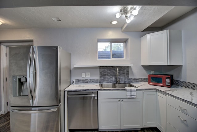 kitchen with sink, appliances with stainless steel finishes, white cabinetry, light stone countertops, and a textured ceiling