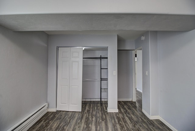 unfurnished bedroom featuring a closet, a barn door, dark hardwood / wood-style floors, and baseboard heating