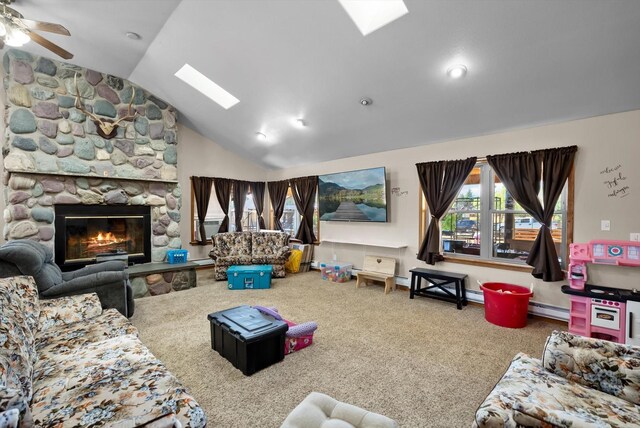 carpeted living room with baseboard heating, ceiling fan, lofted ceiling with skylight, and a fireplace