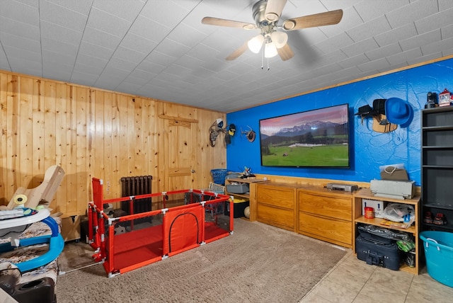 interior space with ceiling fan, light tile patterned floors, wood walls, and radiator heating unit