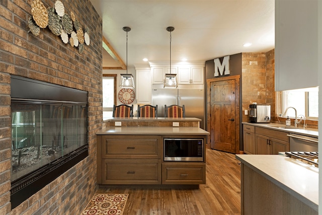 kitchen featuring hanging light fixtures, dark hardwood / wood-style floors, built in appliances, a center island, and brick wall