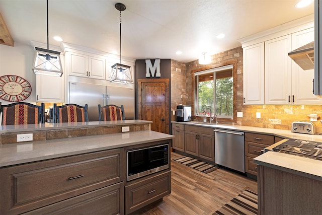 kitchen with built in appliances, white cabinetry, sink, dark wood-type flooring, and decorative light fixtures