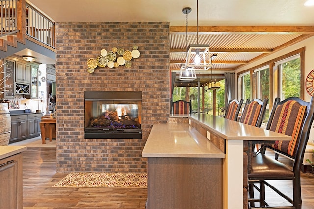 kitchen with light wood-type flooring, pendant lighting, a brick fireplace, a kitchen bar, and brick wall