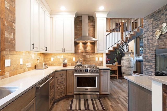 kitchen featuring decorative backsplash, dark wood-style floors, appliances with stainless steel finishes, light countertops, and wall chimney range hood