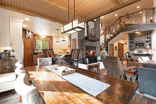 dining area featuring a stone fireplace, wood ceiling, wood-type flooring, a high ceiling, and beamed ceiling