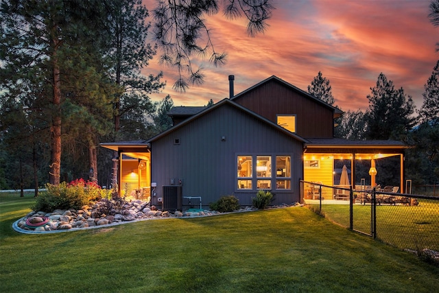 back of house at dusk featuring cooling unit, a yard, and fence