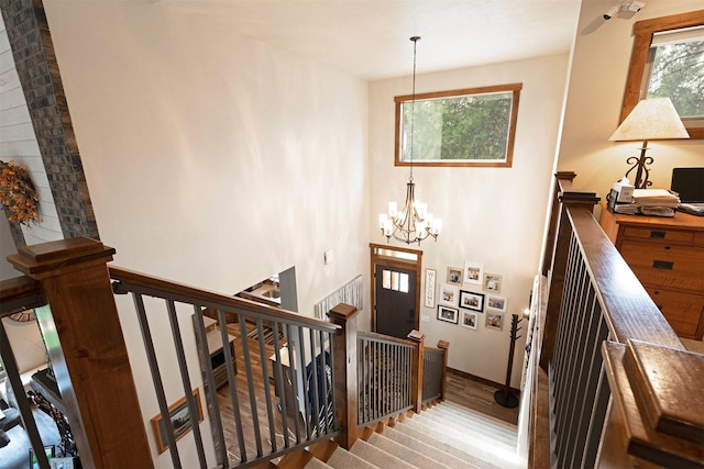 stairway with a high ceiling, a chandelier, and wood finished floors