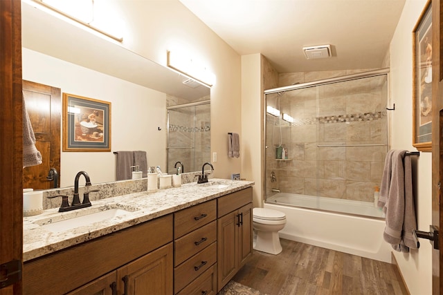 full bathroom with double sink vanity, toilet, wood-type flooring, and enclosed tub / shower combo