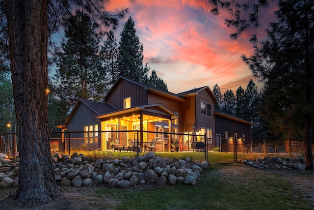 back of house at dusk featuring a yard, fence, and board and batten siding