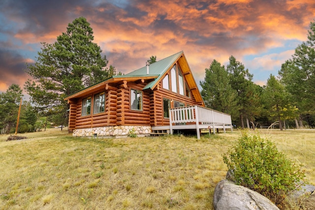 back of property at dusk featuring metal roof, a yard, log exterior, and a deck