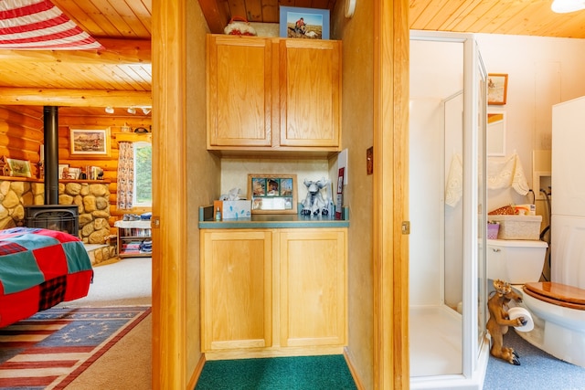 interior space with wooden ceiling, light brown cabinets, log walls, a wood stove, and carpet flooring