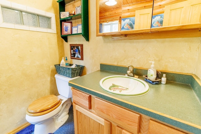 bathroom with a textured wall, vanity, and toilet