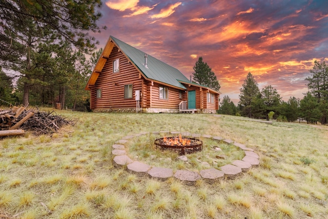 back of house at dusk with a fire pit and log siding