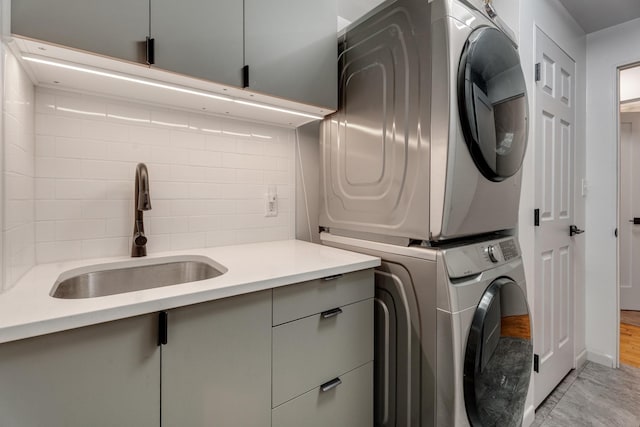 clothes washing area with cabinets, stacked washer / drying machine, and sink