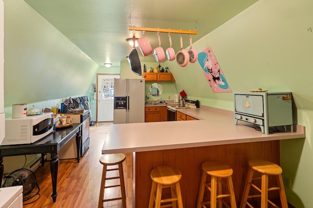 kitchen featuring white appliances, light hardwood / wood-style flooring, a breakfast bar area, and kitchen peninsula