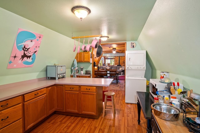 kitchen with light hardwood / wood-style flooring, a breakfast bar area, ceiling fan, stacked washer and clothes dryer, and kitchen peninsula