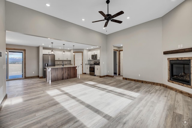 unfurnished living room featuring a high ceiling, light hardwood / wood-style flooring, ceiling fan, and sink