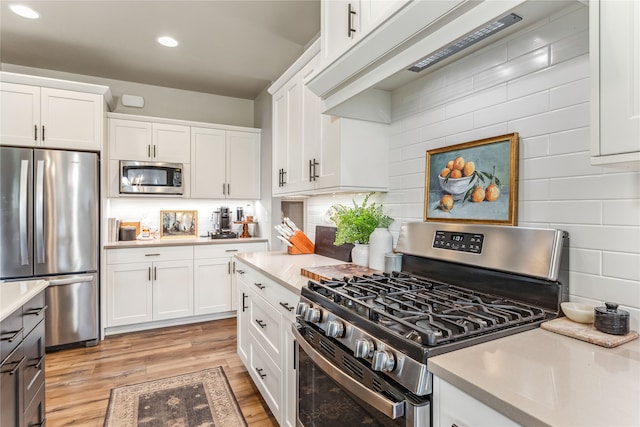 kitchen with light hardwood / wood-style flooring, white cabinetry, ventilation hood, appliances with stainless steel finishes, and decorative backsplash