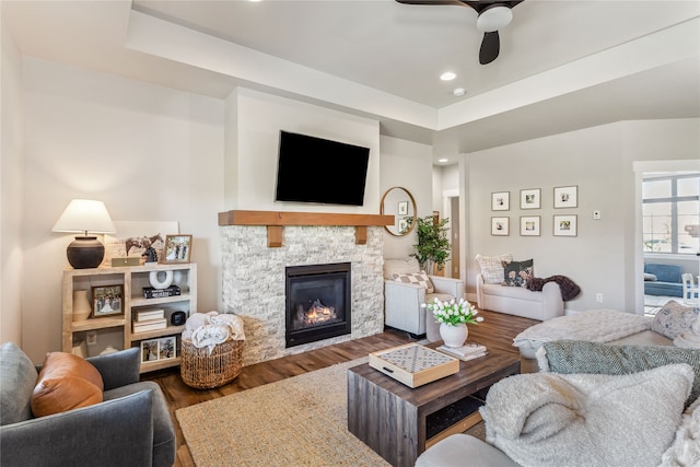 living room featuring ceiling fan, a fireplace, hardwood / wood-style floors, and a tray ceiling