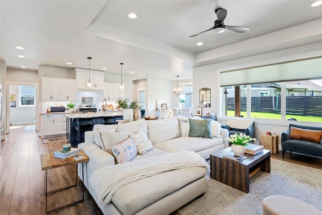 living room with ceiling fan with notable chandelier, sink, and light hardwood / wood-style floors