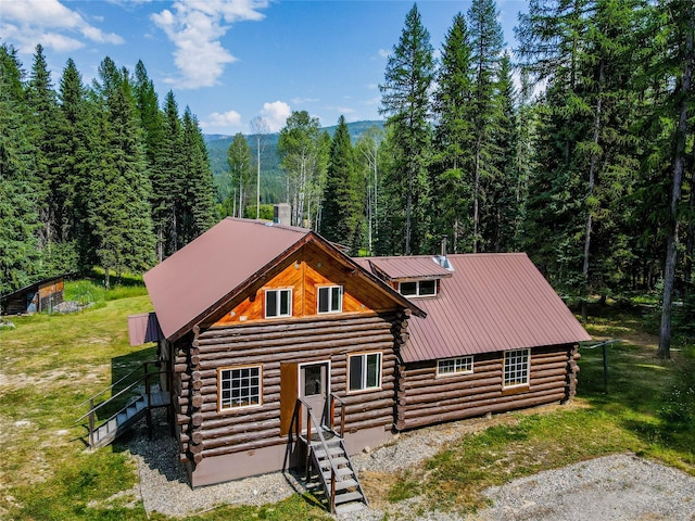 log cabin with log siding, metal roof, a wooded view, and a front yard