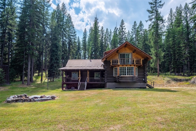 view of front of property featuring log exterior, a balcony, metal roof, a front lawn, and a wooded view