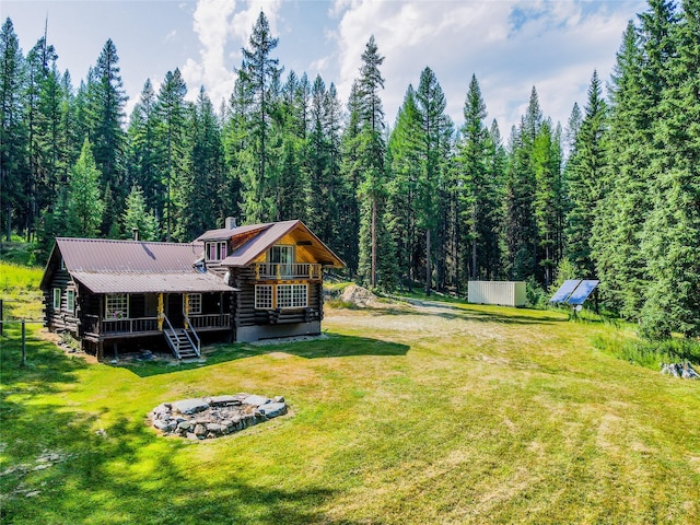 exterior space with log exterior, a forest view, metal roof, a porch, and a front yard