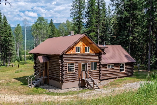 log cabin featuring a forest view, a front lawn, log siding, and metal roof