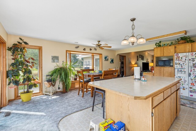 kitchen featuring ceiling fan with notable chandelier, a wealth of natural light, white fridge with ice dispenser, and pendant lighting