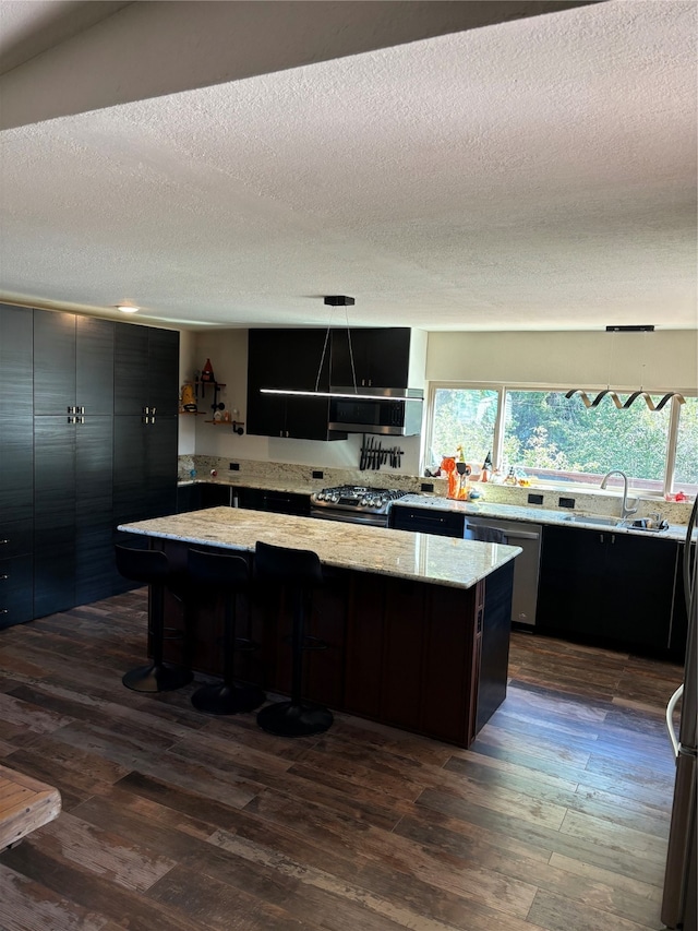 kitchen featuring light stone countertops, pendant lighting, appliances with stainless steel finishes, a center island, and dark wood-type flooring