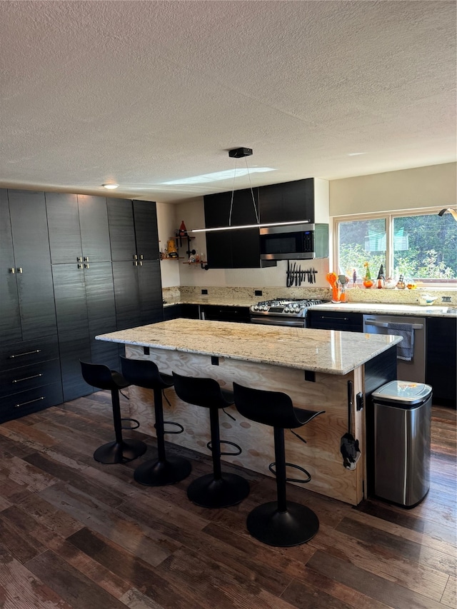 kitchen with a kitchen breakfast bar, decorative light fixtures, dark hardwood / wood-style flooring, appliances with stainless steel finishes, and a center island