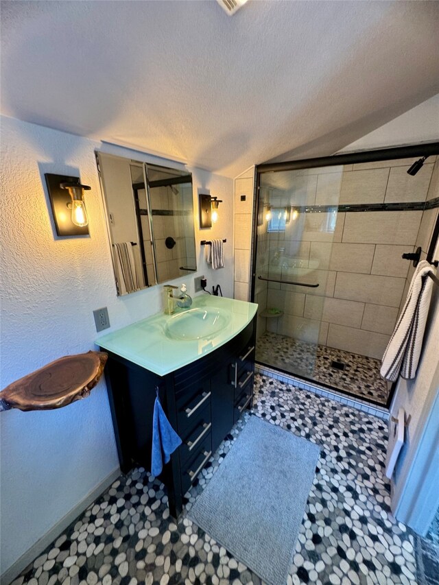 bathroom with a shower with door, vanity, lofted ceiling, and a textured ceiling