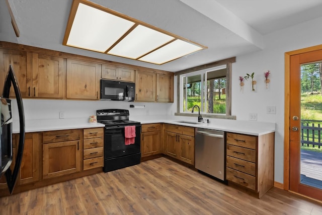 kitchen with light countertops, brown cabinetry, a sink, wood finished floors, and black appliances