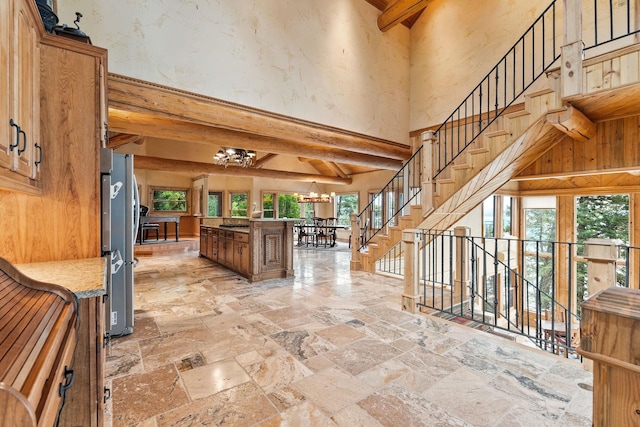 interior space featuring a chandelier, beam ceiling, stone tile floors, and a wealth of natural light