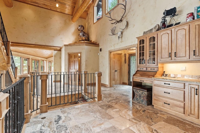 kitchen with stone tile floors, high vaulted ceiling, beam ceiling, wood ceiling, and glass insert cabinets