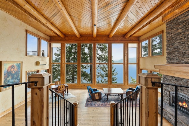 sunroom / solarium featuring beam ceiling, a stone fireplace, wood ceiling, and a water view