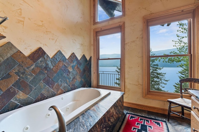 full bathroom featuring a tub with jets, baseboards, wallpapered walls, stone tile flooring, and a water view